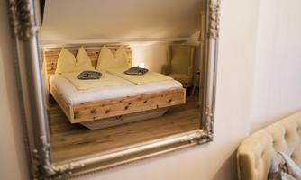 A cozy bedroom with a wooden bed and yellow pillows. The elegant decor can be seen in the mirror.