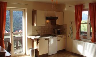 A bright and cozy kitchen with windows and orange curtains. The mountains are visible in the background and the room is well lit.