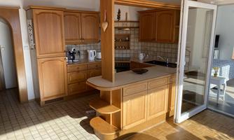 A bright kitchen with wooden cabinets and an open counter. The room has large windows that provide plenty of natural light.