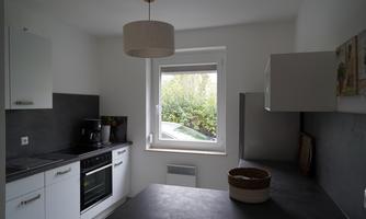 A modern kitchen with white cabinets and a dark countertop. Through the window, the view of the greenery is visible.