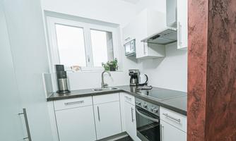 A modern kitchen with white cabinets and an elegant countertop. It includes essential appliances such as a stove and a coffee maker.
