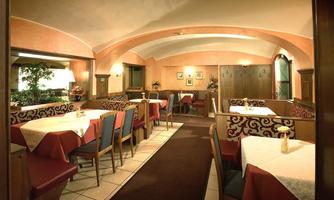 A cozy restaurant with red tablecloths and wooden furniture. The walls are painted in soft colors, and there are plants in the room.