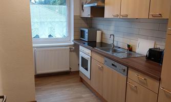 A modern kitchen with light wood cabinets and a large window front. The kitchen is well-equipped with essential appliances such as a stove and microwave.