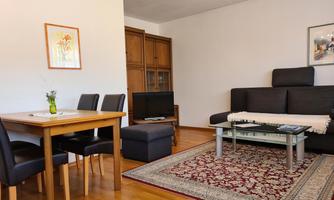 A cozy living room with a black sofa and a wooden table. The room has a rug and a modern decor.