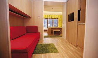 A modern room with a red sofa and a wooden wardrobe. Large windows let in plenty of light and offer a view of the surroundings.