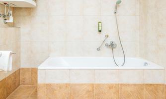 A clean bathroom with a white bathtub and a shower head. The tiles are in neutral colors.