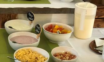A breakfast buffet with various bowls full of muesli, yogurt, and fresh fruit. There are also jams and juices on a green tablecloth.