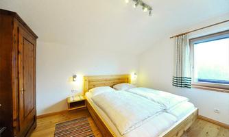 A cozy bedroom with a double bed and wood paneling. Large windows provide plenty of daylight.