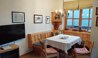 A cozy kitchen with a large table and wooden bench. The room is bright and has windows with a view outside.
