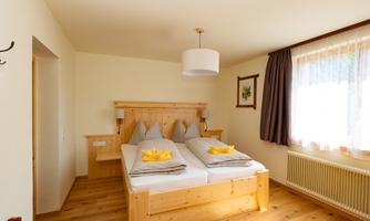 A bright guest room with two single beds and wood details. Large windows provide plenty of daylight and a cozy atmosphere.