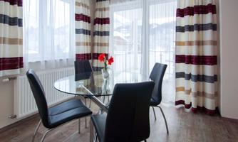 A stylish dining area with a round glass table and four black chairs. Large windows let in plenty of light and the curtains have a modern striped design.