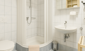 A modern bathroom with a shower cubicle, sink, and toilet. The walls are tiled and the room appears bright and clean.