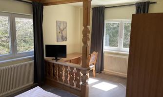 A bright room with a wooden railing, a table, and a television. Large windows provide plenty of light and a view of nature.