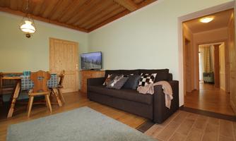A cozy living room with a dark brown sofa and a wooden table. The walls are light green, and a large rug is on the floor.