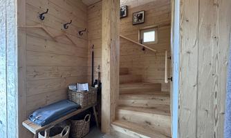 An inviting wooden entrance area with a staircase and a bench. Coat hooks hang on the wall, and there are baskets for additional storage.