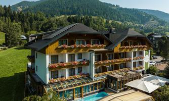 A beautiful hotel with a swimming pool and balconies. The picturesque surroundings are surrounded by mountains and forests.