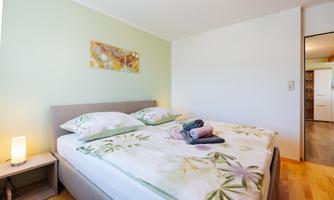 A cozy bedroom with a double bed and green wall design. A lamp is on the nightstand and fresh towels are lying on the bed.