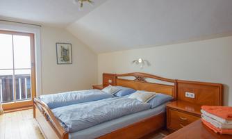 A cozy bedroom with two single beds and a wooden shelf. The room is brightly lit and has a balcony for the view.
