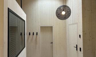 A modern entrance area with bright wooden surfaces and a large window. A decorative lamp hangs from the ceiling, providing cozy light.