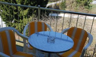 A balcony with two comfortable chairs in orange and white, as well as a round table. In the background, trees and a quiet landscape can be seen.