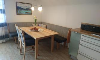 A cozy dining area with a wooden table and benches. On the table, there is fresh fruit and a flower vase.