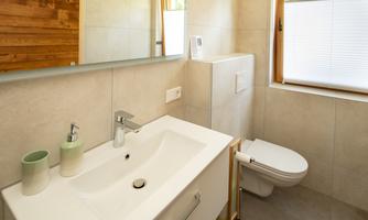 A modern bathroom with a white sink and a toilet. The room has light tiles and a window that provides daylight.