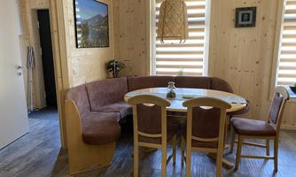 A cozy dining area in a wooden house. It consists of a round table and a bench, surrounded by atmospheric lighting and wood paneling.