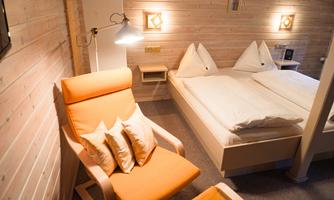 A cozy bedroom with a double bed and two pillows. An orange armchair next to the bed creates an inviting atmosphere.