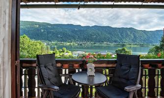 A cozy balcony with two chairs and a table. In the background, there is a beautiful view of a lake and the mountains.