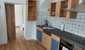 A modern kitchen with wooden shelves and white tiles. The room is bright and friendly with plenty of storage space.