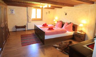 A cozy bedroom with two beds and red pillows. The room is equipped with wooden paneling and warm light.