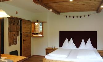 A cozy bedroom with wooden décor and a double bed. The room has a warm atmosphere and large windows for natural light.