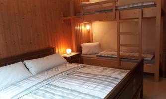 A cozy bedroom with a double bed and a wooden bunk bed. The walls are made of wood and there is soft lighting.