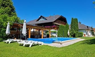 A beautiful garden with a pool and loungers. In the background, there is a cozy house under a blue sky.