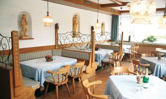 A cozy restaurant with bright tablecloths and wooden chairs. The walls are decorated with decorative statues and there are different seating areas.