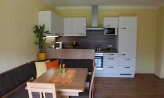 A modern kitchen with a dining area and a cozy seating corner. The walls are painted in soft colors and there are plants for decoration.
