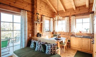 A cozy wooden house with large windows and bright wood interiors. The open kitchen and dining area create an inviting atmosphere.
