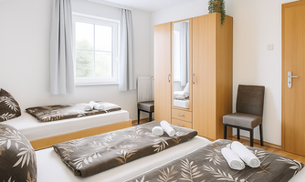 A cozy bedroom with two single beds and a chair. The room has bright colors and large windows that let in plenty of light.
