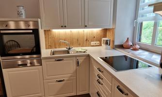 A modern kitchen with white cabinets and wooden details. It is well-lit and features a stove as well as a sink.