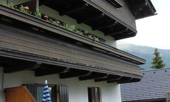 A traditional wooden house with a balcony and flowers. In the foreground, there is a small garden with a table and chairs.