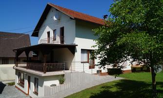 A modern house with a balcony and a green lawn. Other buildings can be seen in the background.