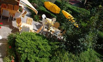 A cozy outdoor area with yellow umbrellas and tables. Lush greenery and colorful flowers create an inviting atmosphere.