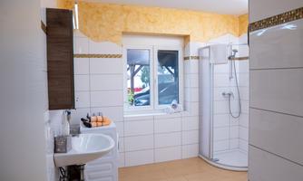 A modern bathroom with a shower and a sink. The walls are brightly tiled and there is a window with a view outside.