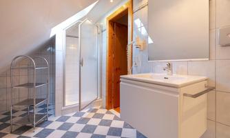 A modern bathroom with a shower area and a large mirror. The floor is designed with black and white tiles, and there is a space-saving shelving unit.