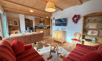 A cozy living room with red sofas and a wooden table. The decoration is rustic and the atmosphere is inviting.