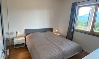 A cozy bedroom with a double bed and a window overlooking the mountains. The room has a modern style and warm lighting.
