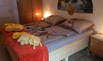 A cozy bedroom with a double bed covered in animal motifs. On the bed are yellow and red towels, as well as a wooden dresser in the background.
