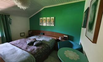 A cozy bedroom with a large bed and green-painted walls. There is a table and a chair in the corner, as well as decorative pictures on the wall.