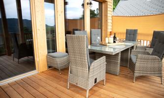 An inviting terrace area with a glass table and comfortable seating made of woven material. The wooden cladding and the view of the surrounding nature create a cozy atmosphere.