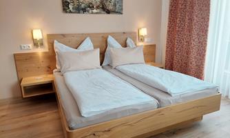 A modern bedroom with two single beds and bright walls. There is a wooden panel above the bed and some decorative elements.
